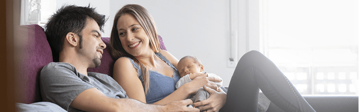 A couple of parents sitting on a sofa in the living room with their newborn baby at home